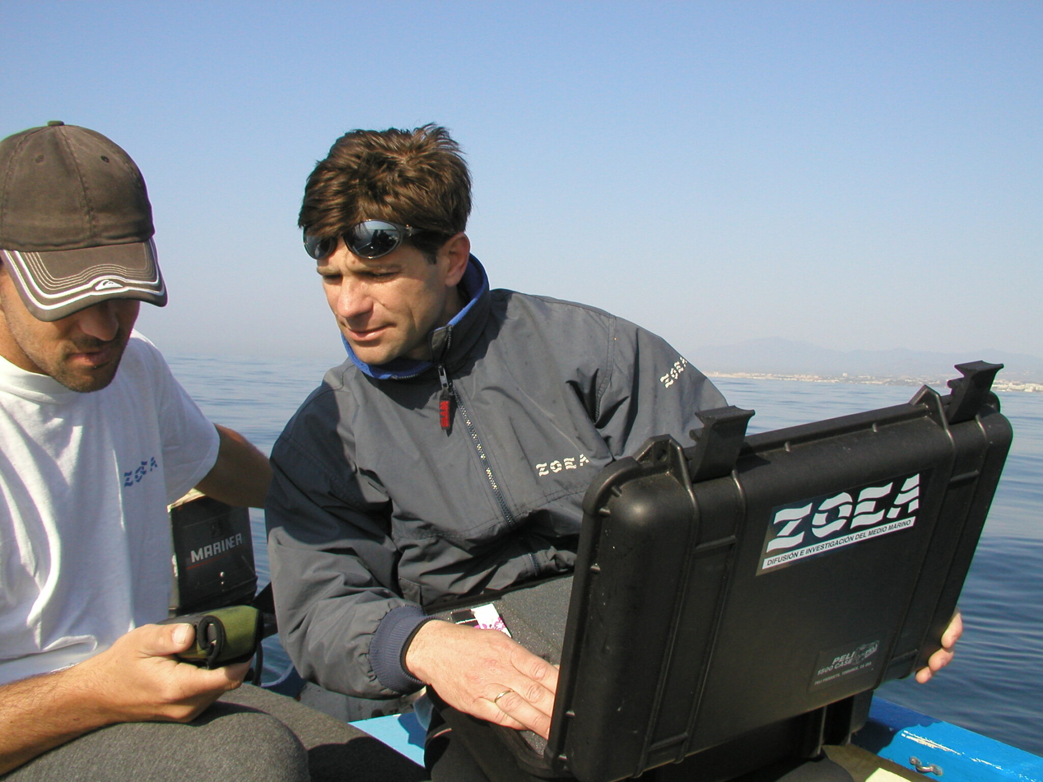 Two divers on a boat looking at a GPS to find the location of a dive site