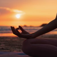 hand of a woman meditating in a yoga pose on the beach at sunset