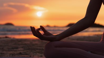 hand of a woman meditating in a yoga pose on the beach at sunset