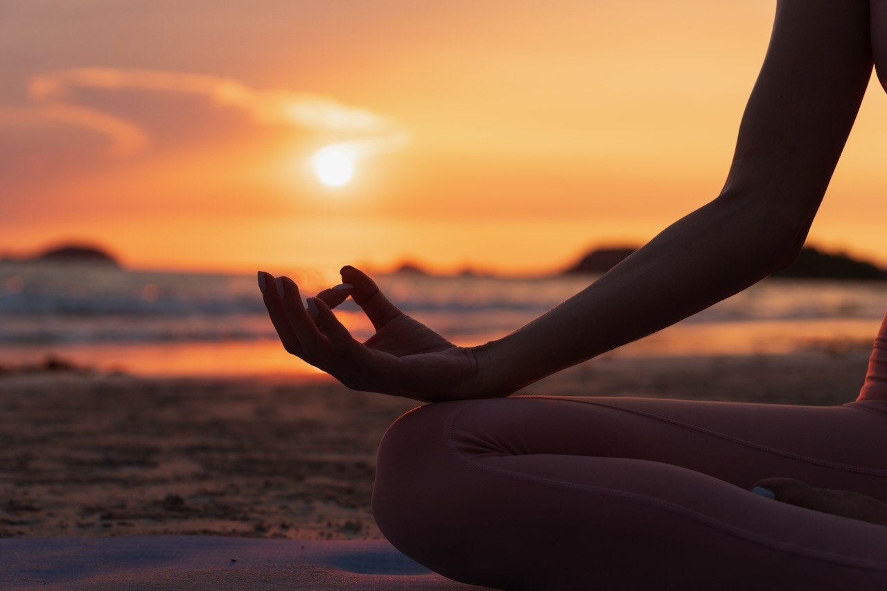 hand of a woman meditating in a yoga pose on the beach at sunset