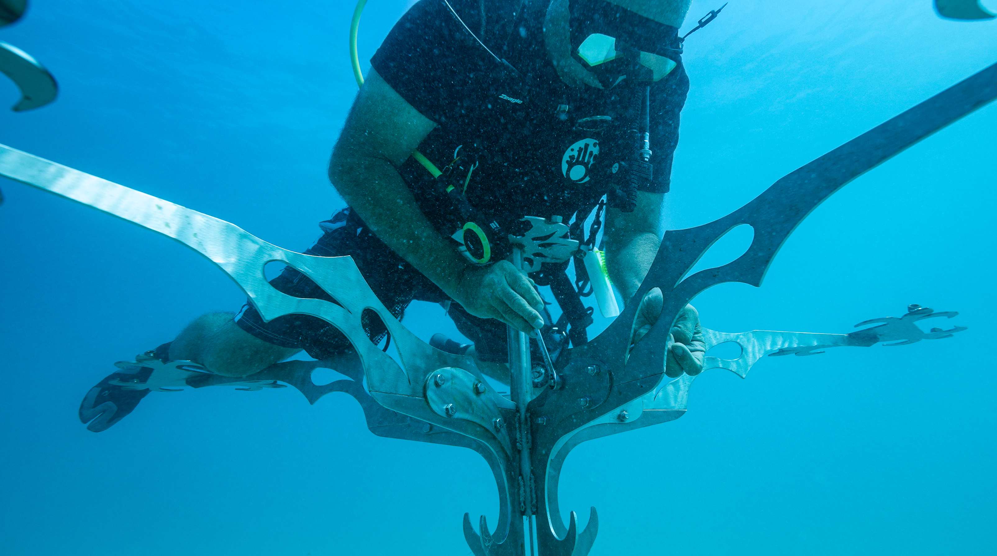 Scuba diver attaching coral to an artificial coral tree on a sandy bottom for Counting Corals restoration project in Fiji