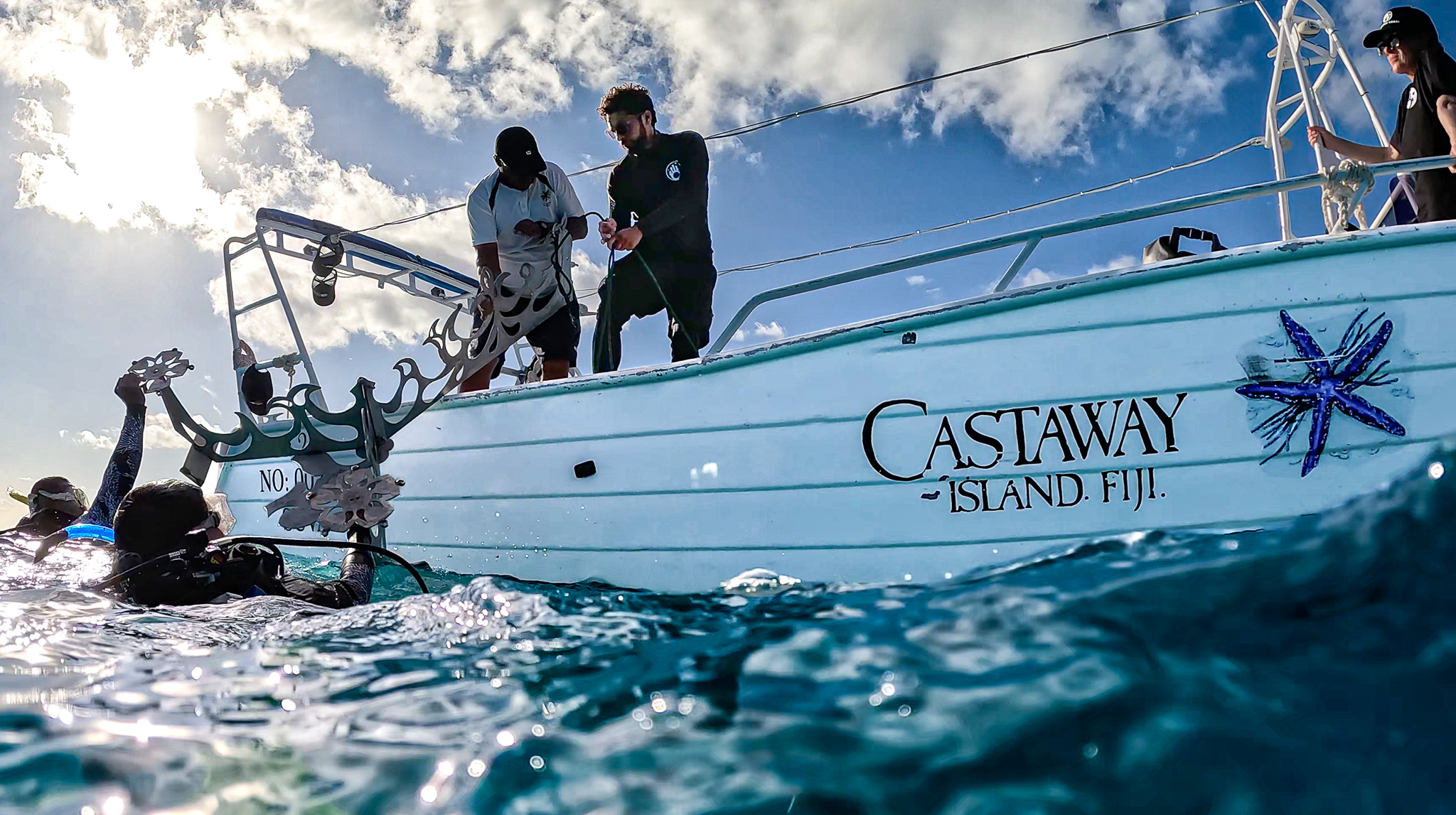 Divers on the side of a boat carrying an artificial coral tree for Counting Corals restoration project in Fiji