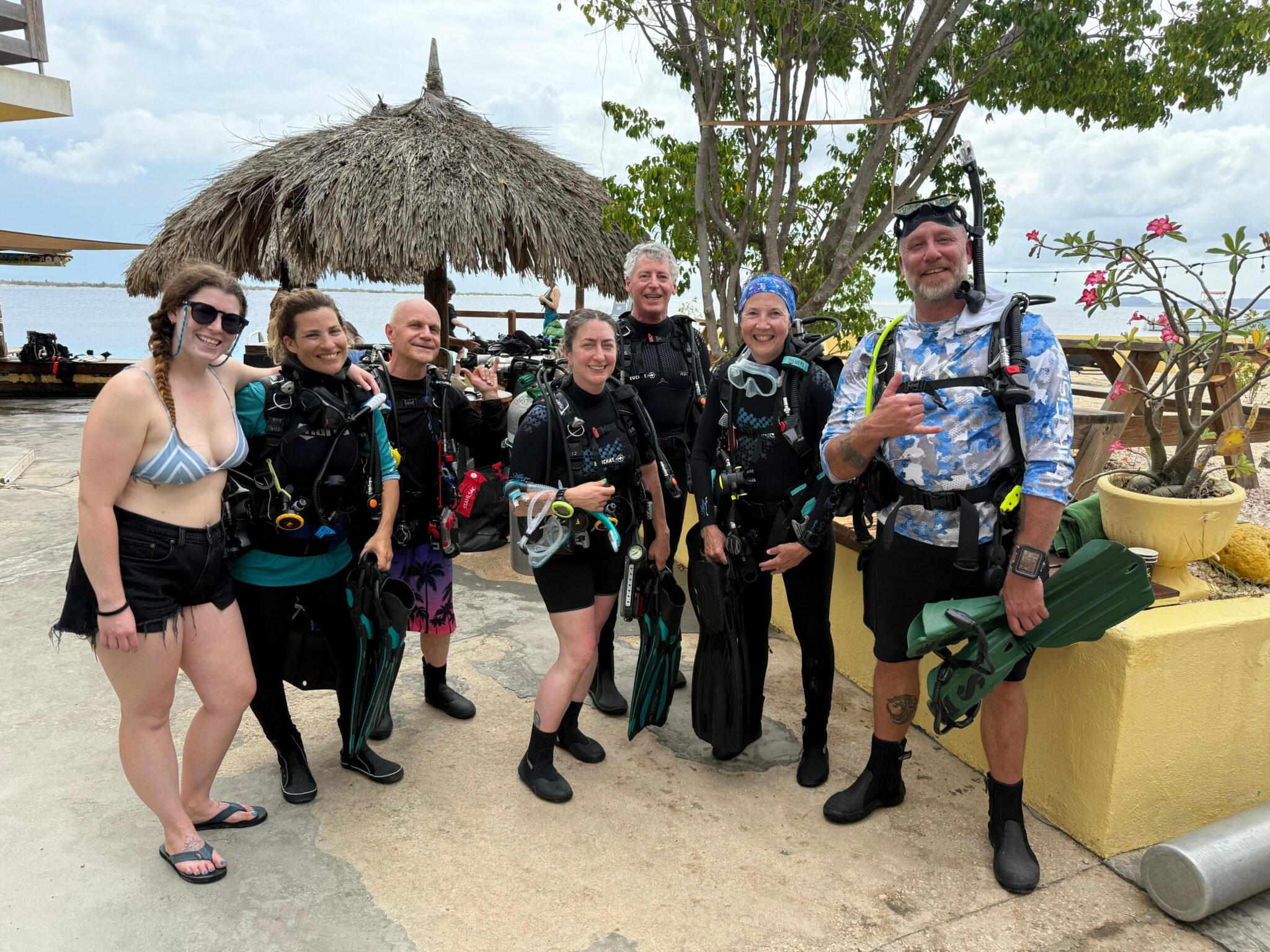 Several divers, all geared up, stand next to a palapa at Buddy Dive in Bonaire