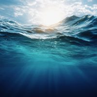 Underwater view of the deep blue ocean, with sunlight filtering through to create ripples and waves. The water is calm yet powerful, representing both depth and serenity.