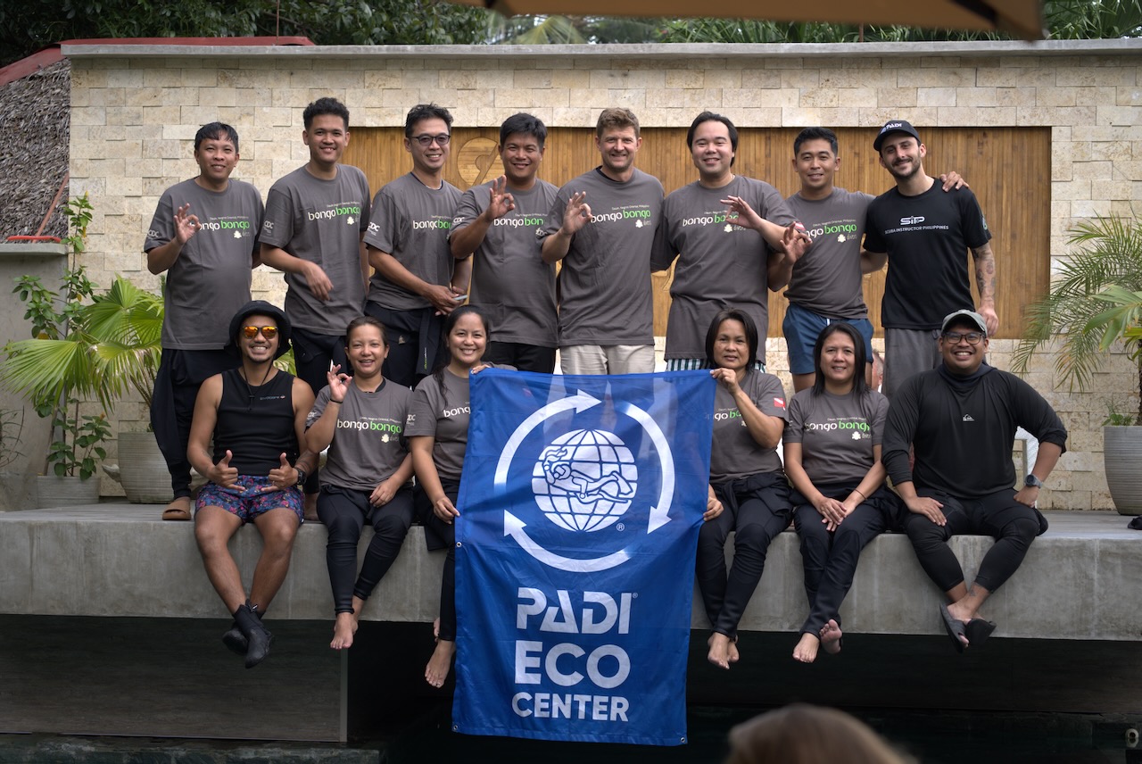 Staff at Bongo Bongo Divers in the Philippines sits on a congret wall and holds a PADI Eco Center flag