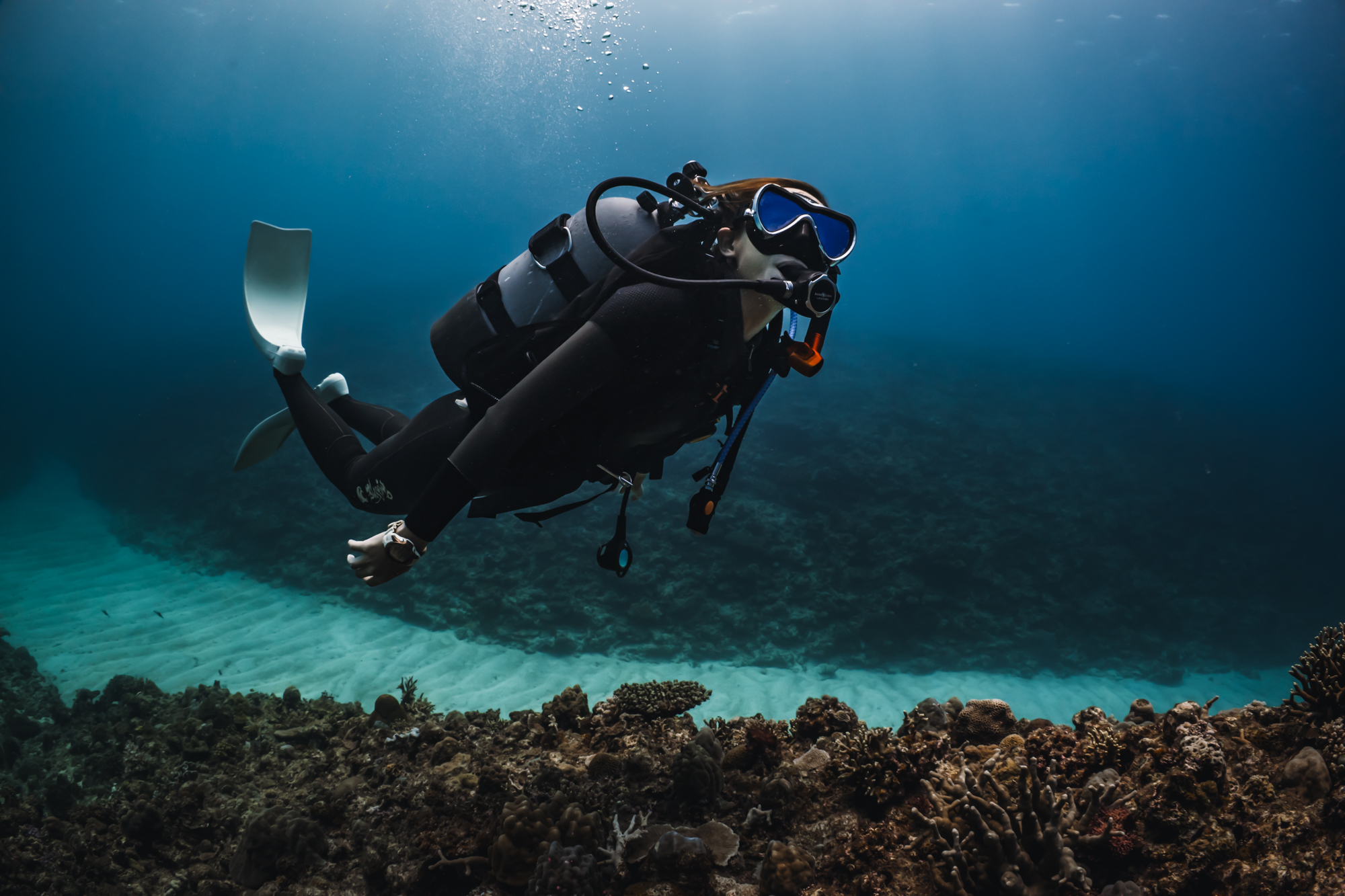 A scuba diver swims underwater, exploring a coral reef in Okinawa, Japan