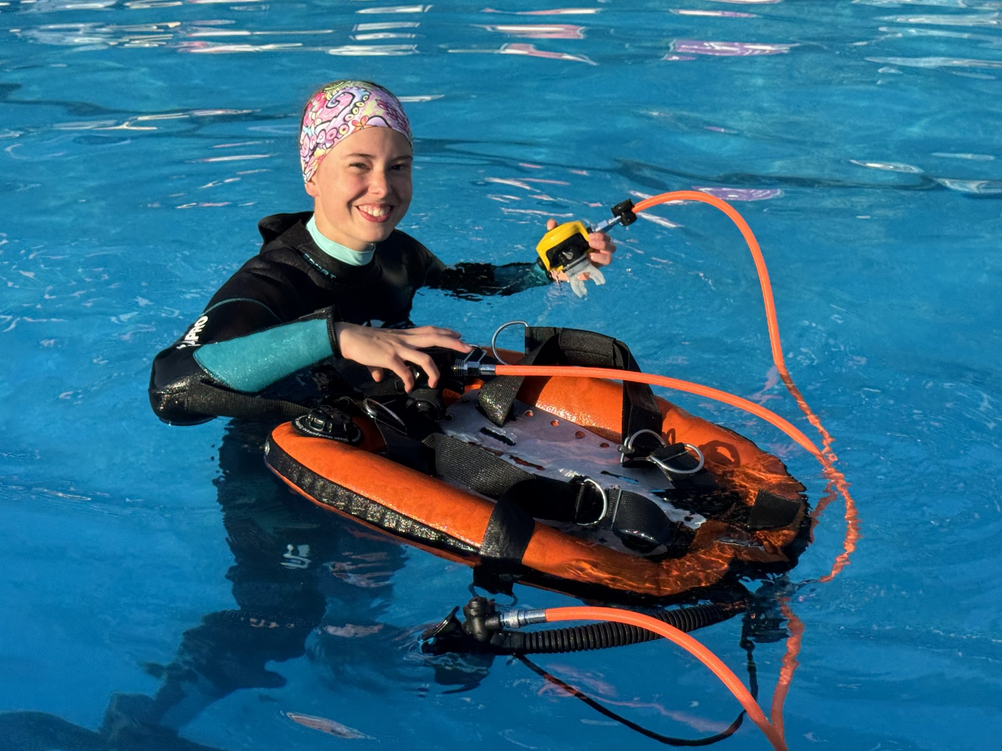 Diver standing in a pool smiling next to her gear with the BCD inflated on the surface