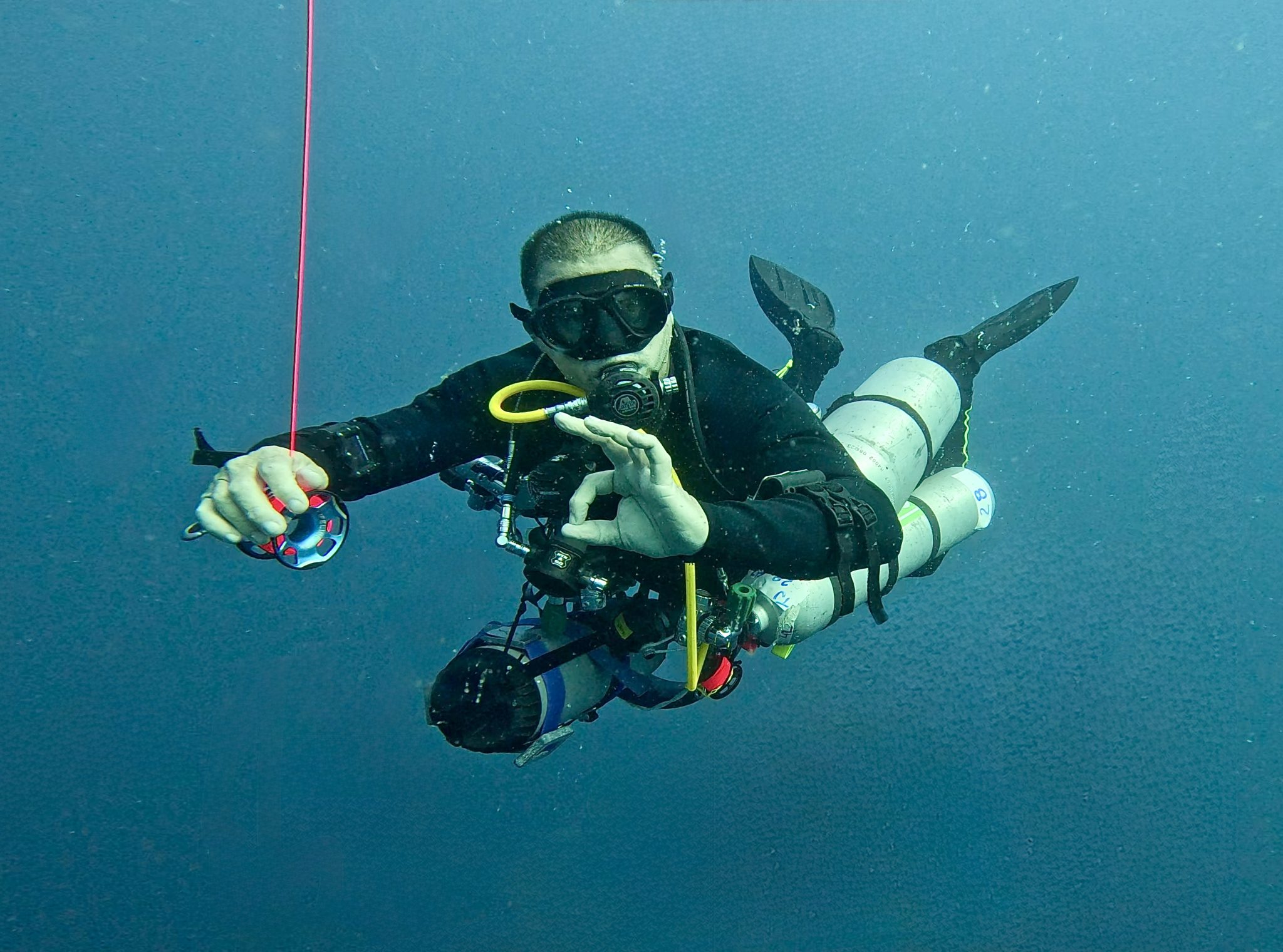 A tec diver with sidemount configuration holding an SMB reel and giving the ok signal