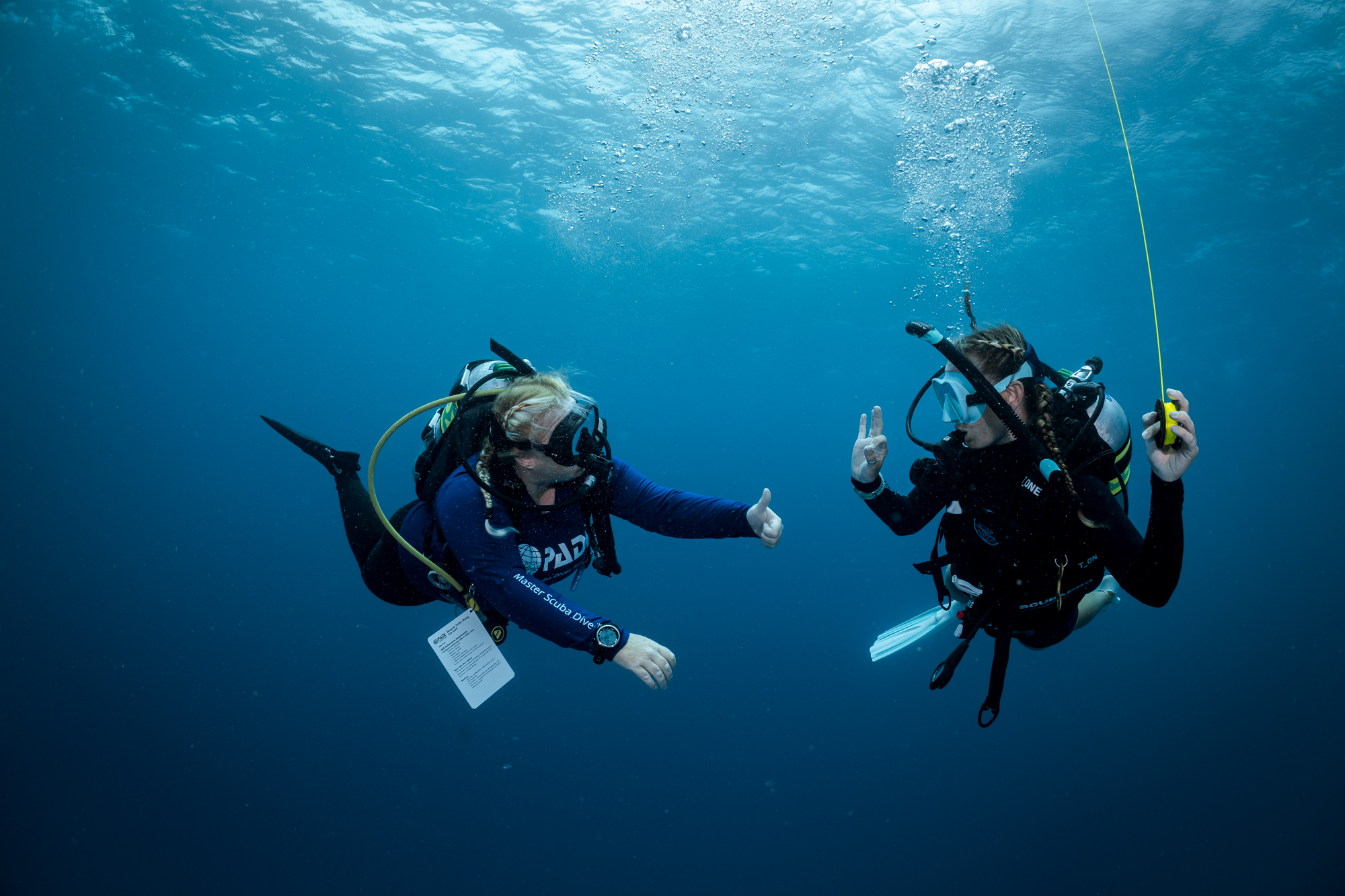 Two divers use hand signals to confirm they are ready to ascend from their dive