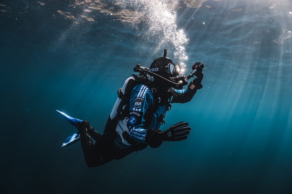 A dry suit divers vents air from their inflator hose while ascending from a cold water dive