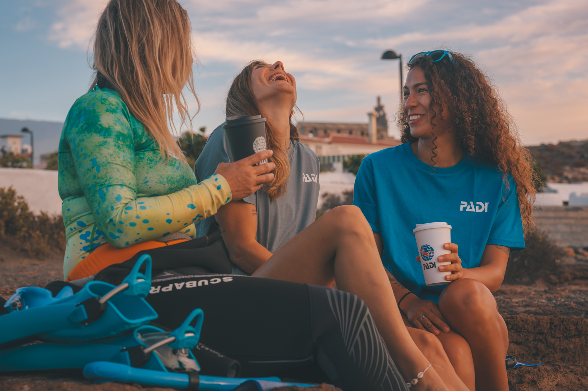 Three women divers laughing on the beach over coffee