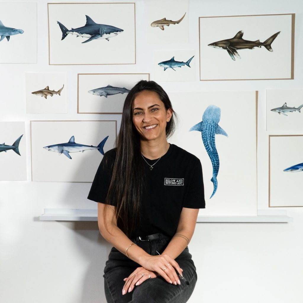 PADI AmbassaDiver Janavi Kramer sits in front of a wall of painted sharks