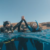 Three women divers high fiving on the surface of the ocean