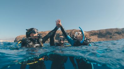 Three women divers high fiving on the surface of the ocean