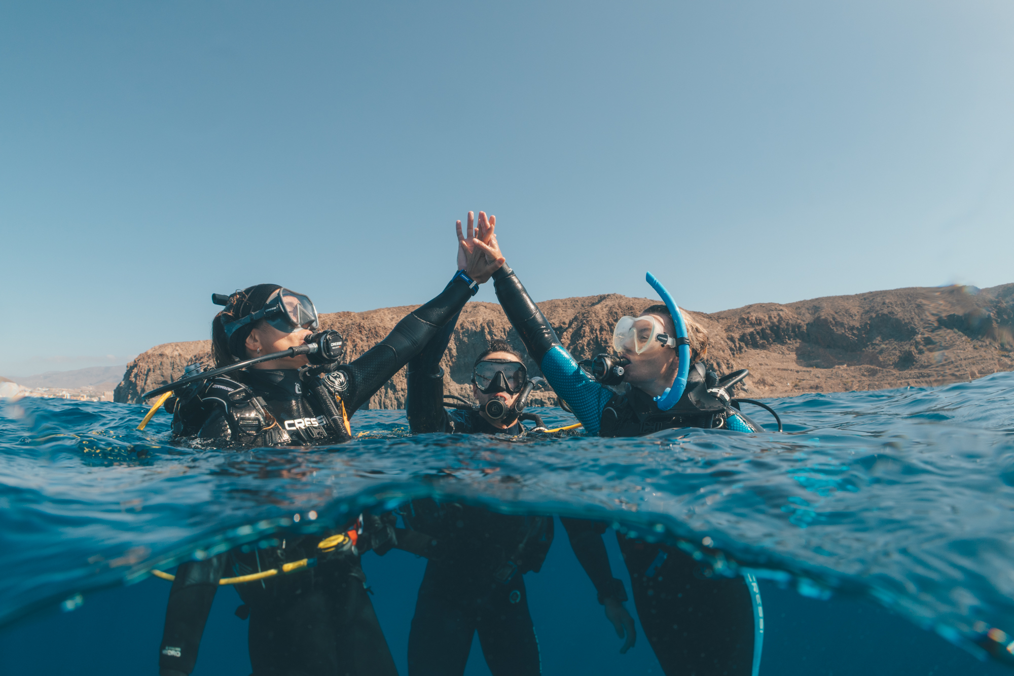 Three women divers high fiving on the surface of the ocean