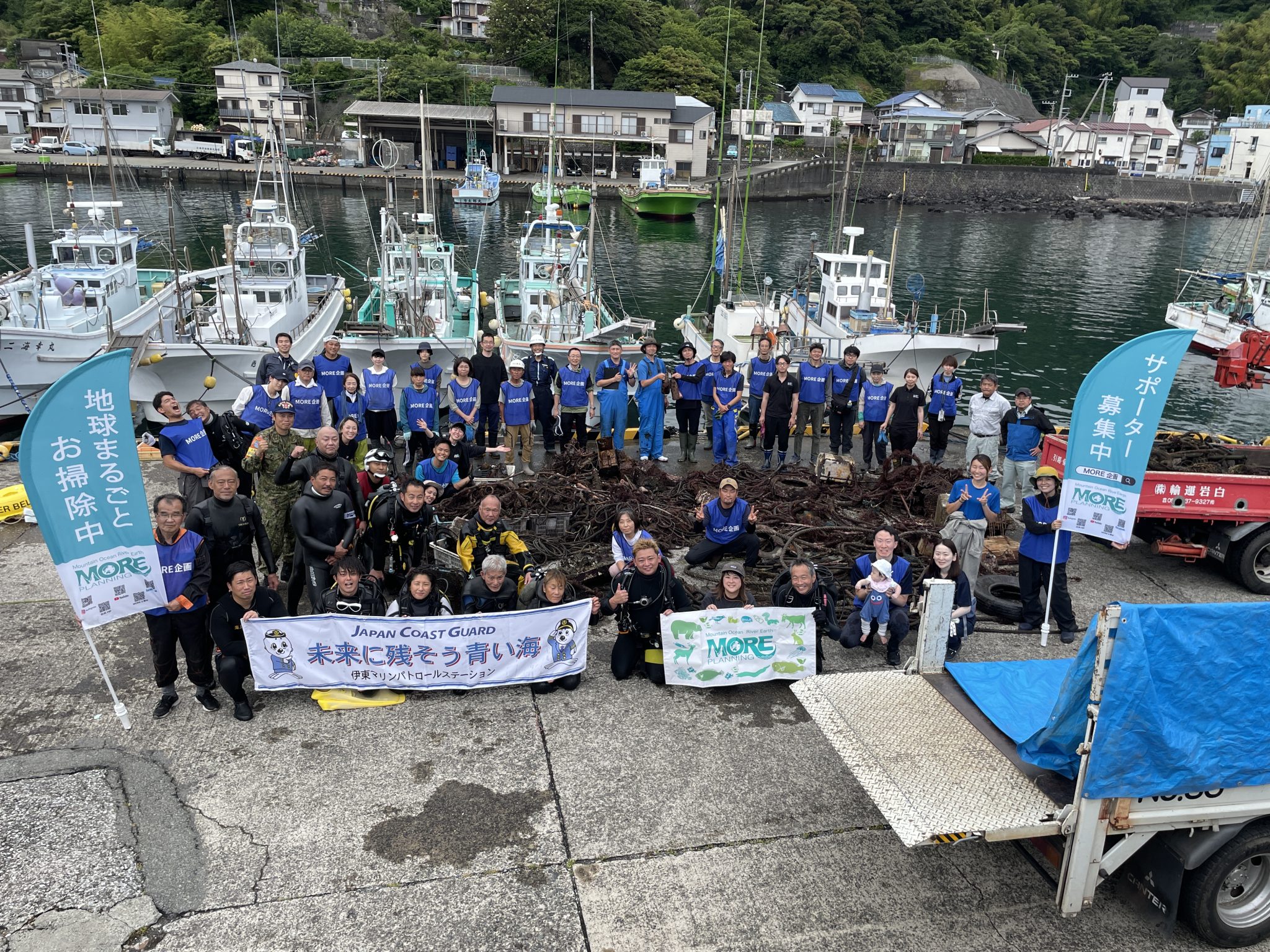 Ambassadiver & Ocean Torchbearer Award winner Yumi Shirai with a large group of MORE school volunteers and divers posing on a dock with huge piles of underwater debris they've collected