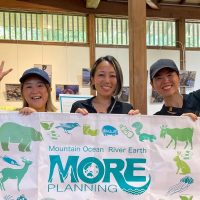 Ambassadiver Yumi Shirai in a classroom holding a sign with two other women for MORE school for conservation