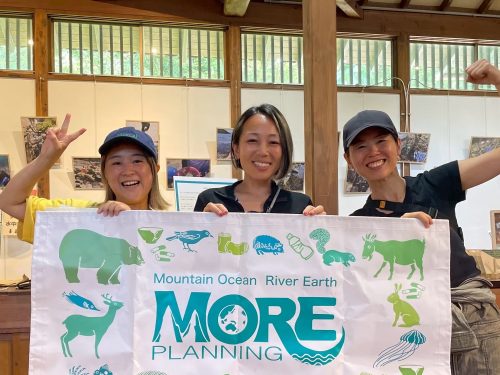 Ambassadiver Yumi Shirai in a classroom holding a sign with two other women for MORE school for conservation